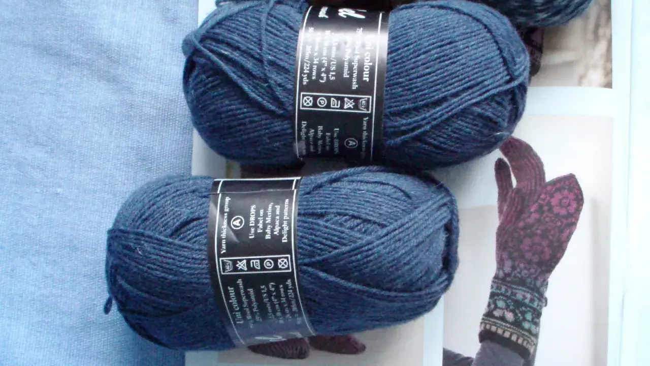 Two balls of dark blue yarn and a knitted glove with a floral pattern.