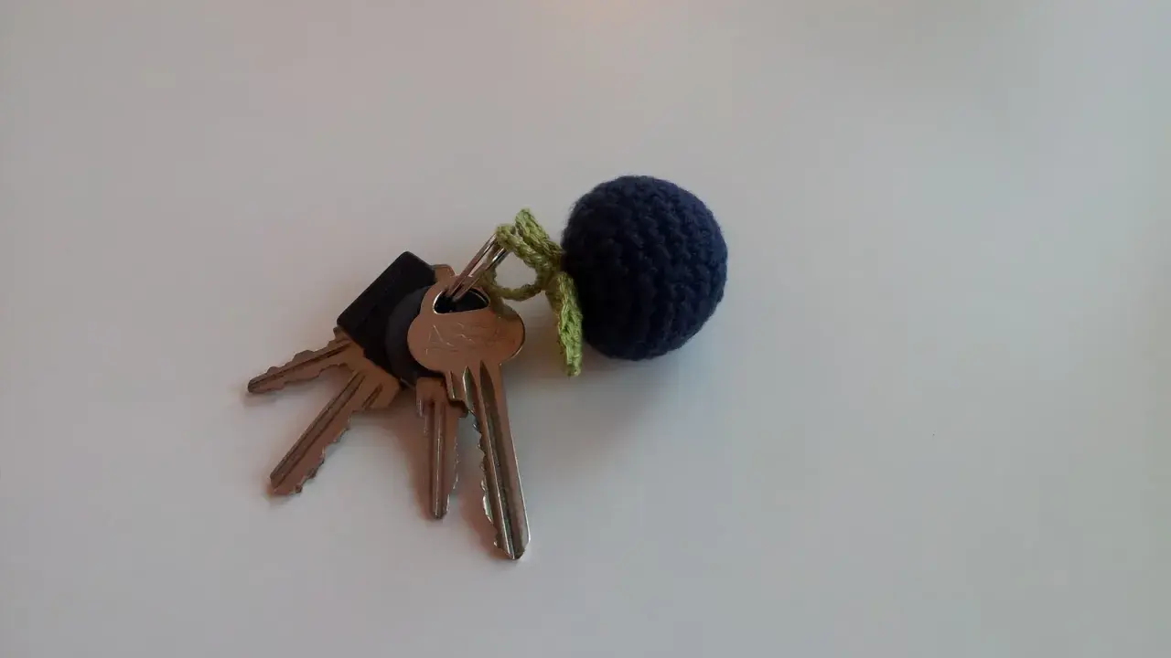 En mörkblå virkad nyckelring i form av ett bär, fäst vid ett knippe nycklar.
