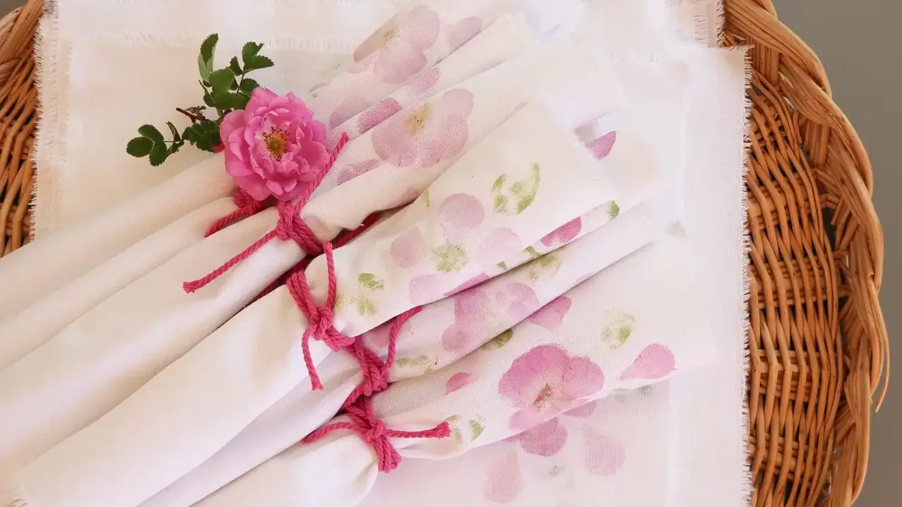 Vita tygservetter med rosa blommor, bundna med rosa snöre och dekorerade med en ros. Vackert dukat för en sommarfest.