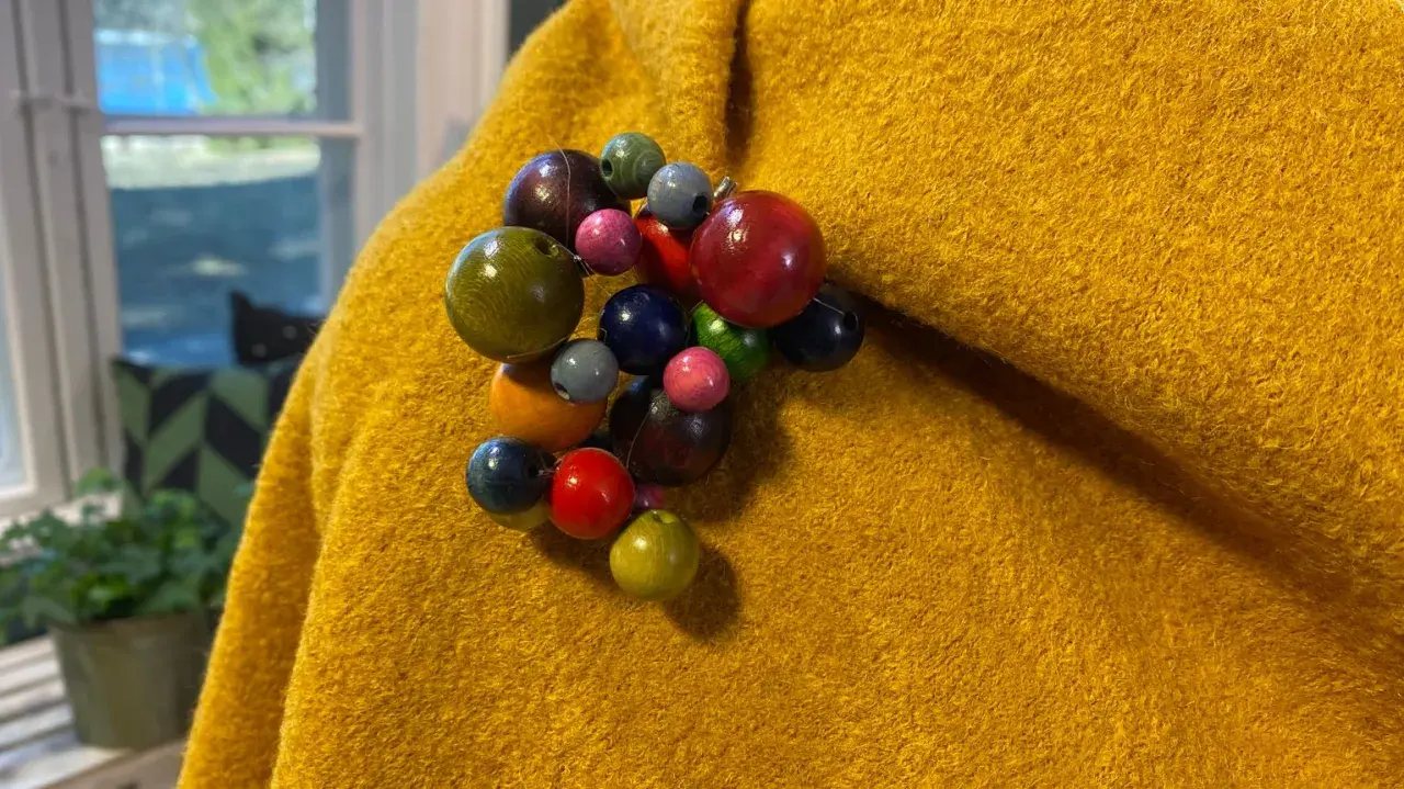 En gul, ullig poncho med en klunga av färgglada träpärlor som en brosch. Perfekt för att sy en unik poncho.