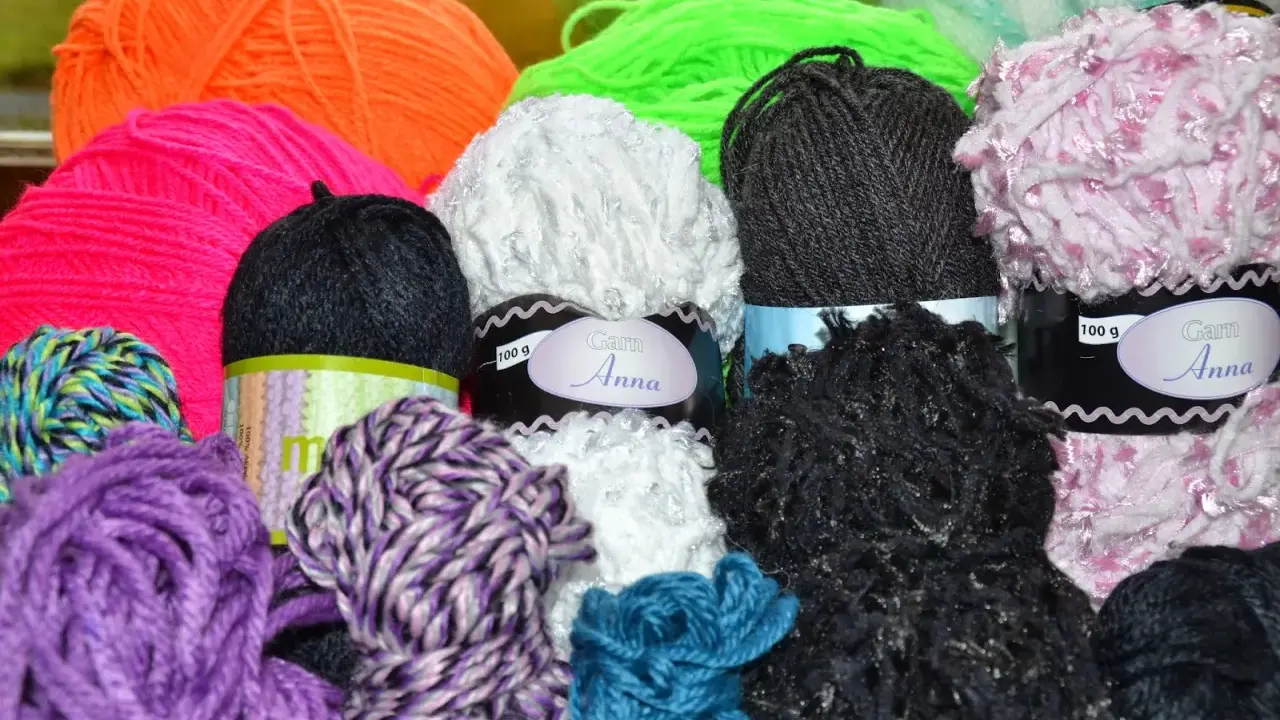 A colorful assortment of yarn balls in various textures and colors, including purple, pink, orange, green, white, black, and blue.