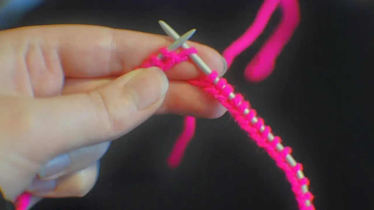En hand håller stickor och ljusrosa garn, redo att starta stickning.