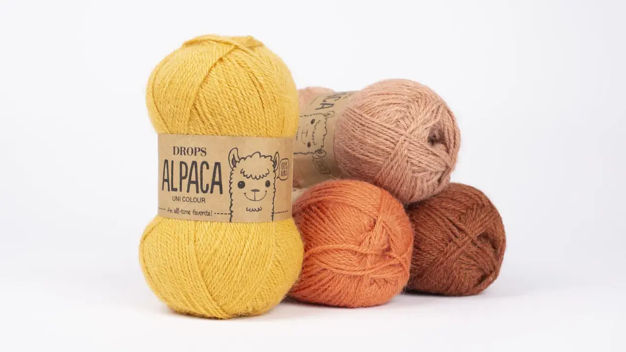 Garnnystan i varma färger som ockra, orange och rost. En guldig nystan från Drops Alpaca har en söt alpacka på etiketten.