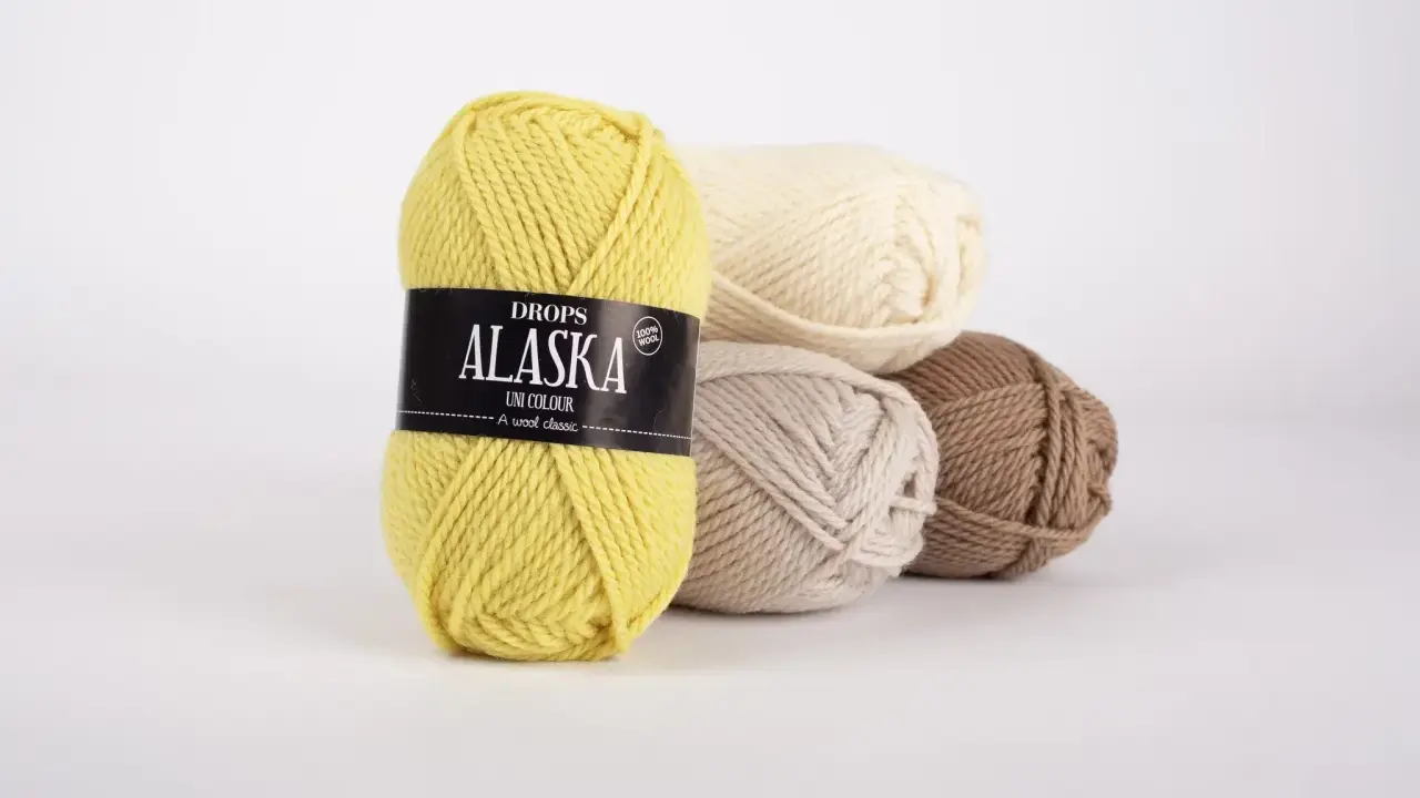 Gula, beige, ljusbruna och vita nystan av Drops Alaska garn ligger i en hög.