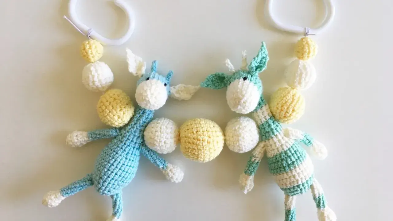 Crocheted giraffes with white and yellow beads hanging from white plastic rings.