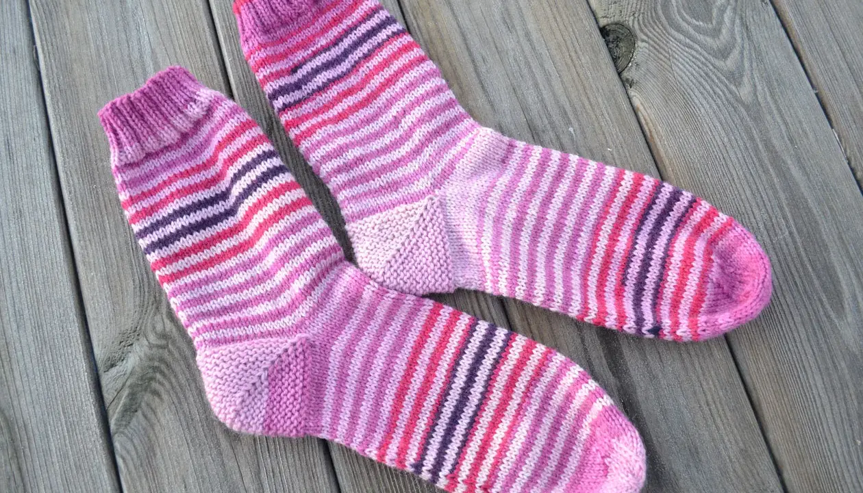 Två par randiga sockor i rosa och lila toner ligger på en träyta.