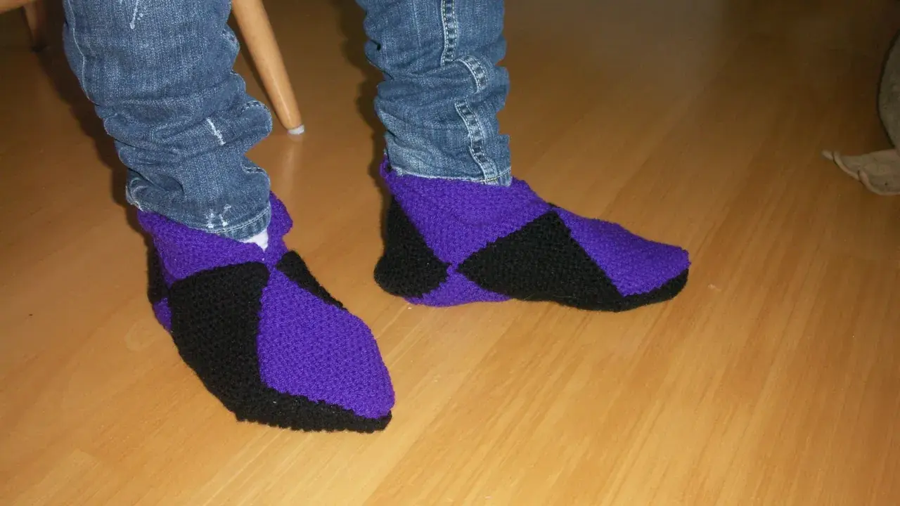 Ett par stickade innetofflor i lila och svart, med jeans till. Perfekta för mysiga hemmakvällar.