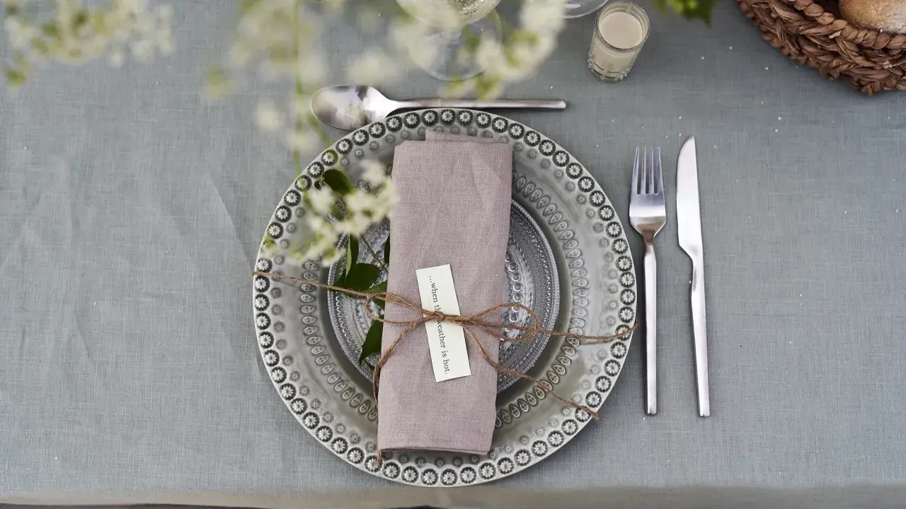 Vacker dukning med linneservetter, blommor och en korg med bröd. Perfekt för en sommarfest.