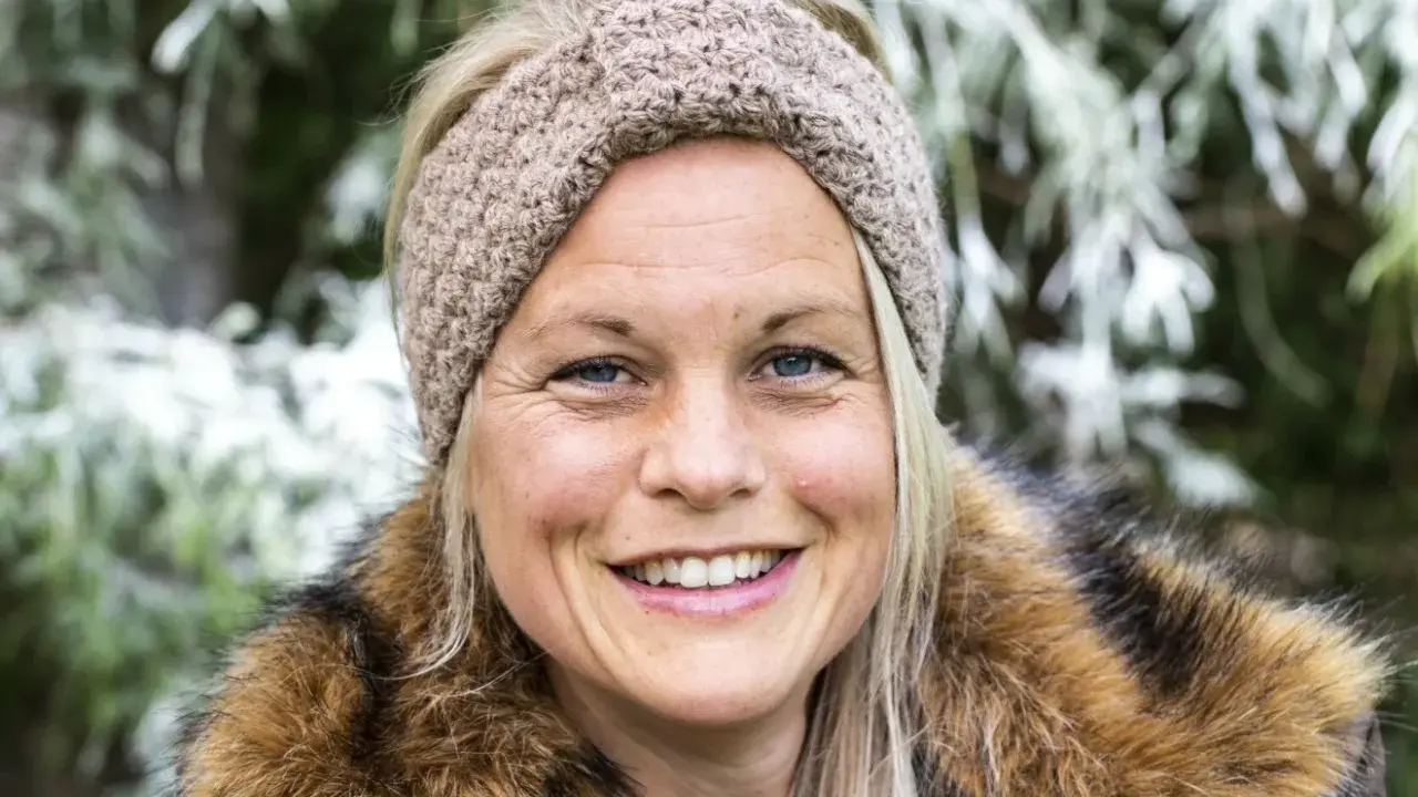 Glad kvinna med virkat pannband med twist och pälskrage, ute i naturen.