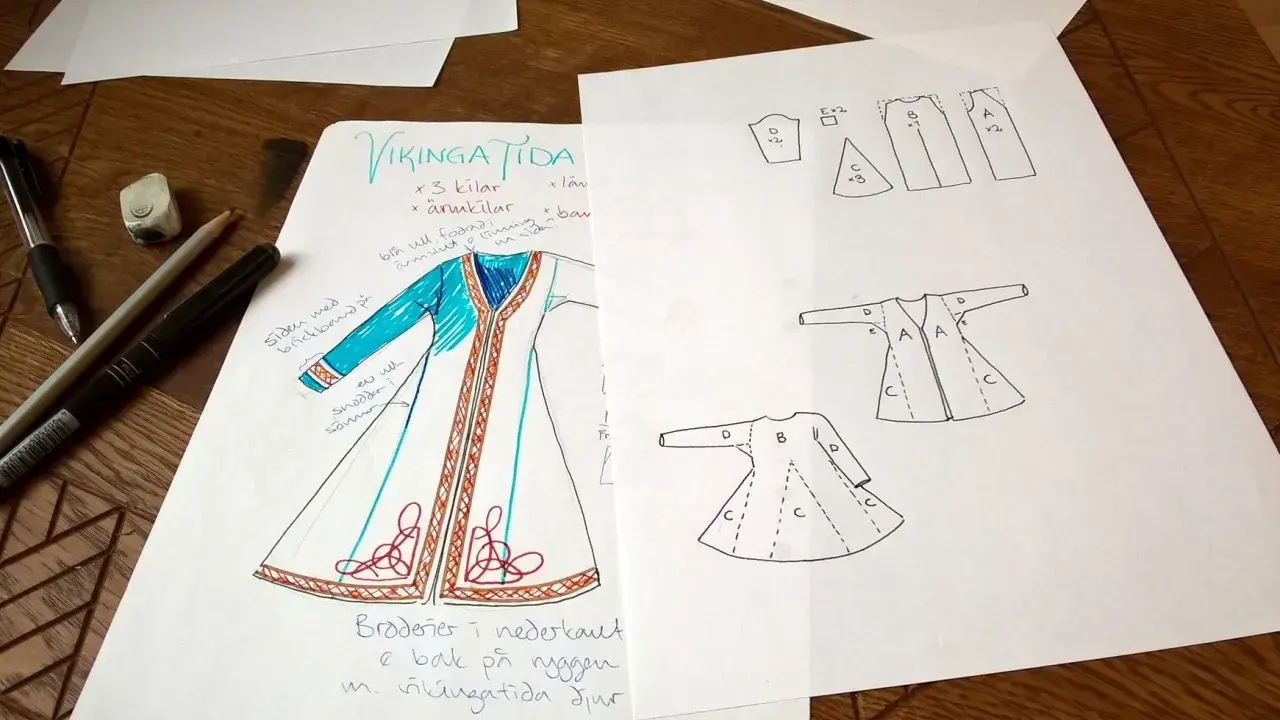 Skisser för en vikingatida kappa med mönster och sömnadsdetaljer. Pennor och suddgummi ligger bredvid.