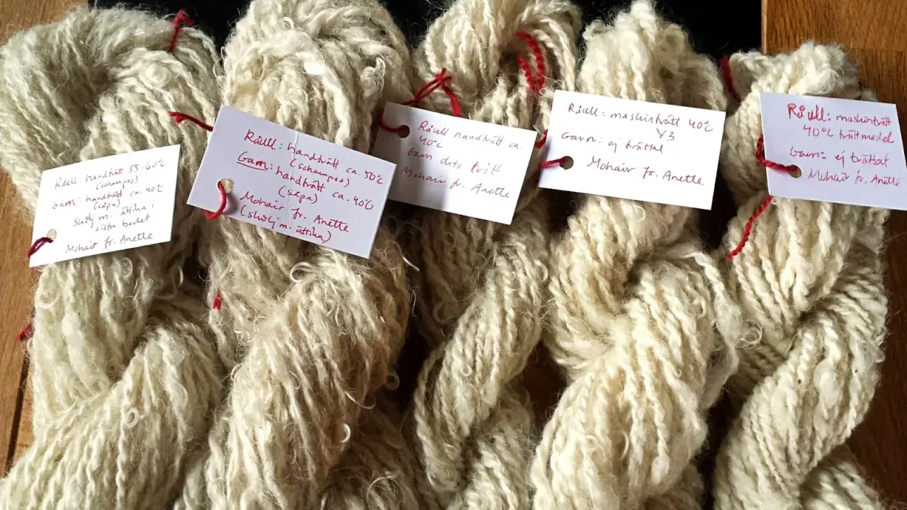 Buntar av ljusbeige garn, troligen mohair ull, med handskrivna etiketter som beskriver tvättmetoder och ursprung.