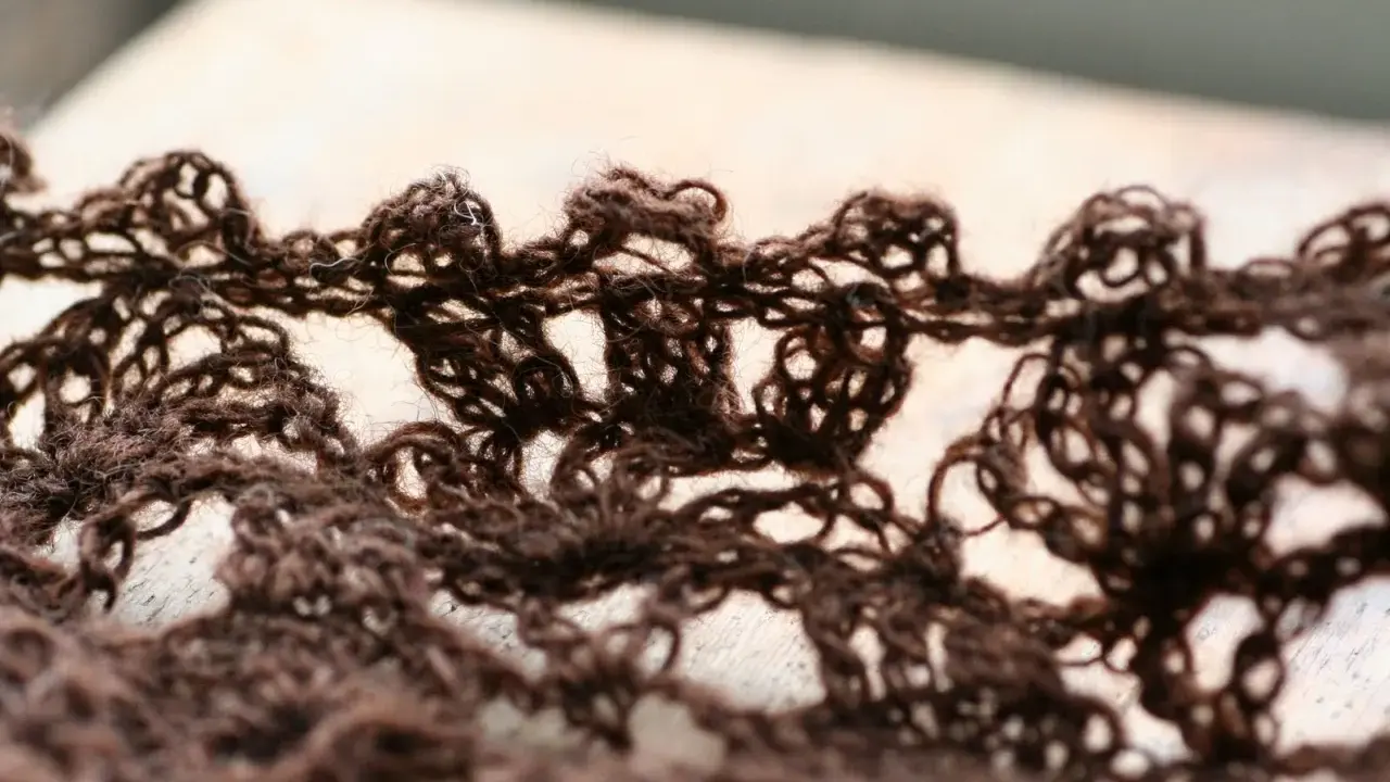 Close-up of a brown, lacy crocheted fabric with an openwork pattern.