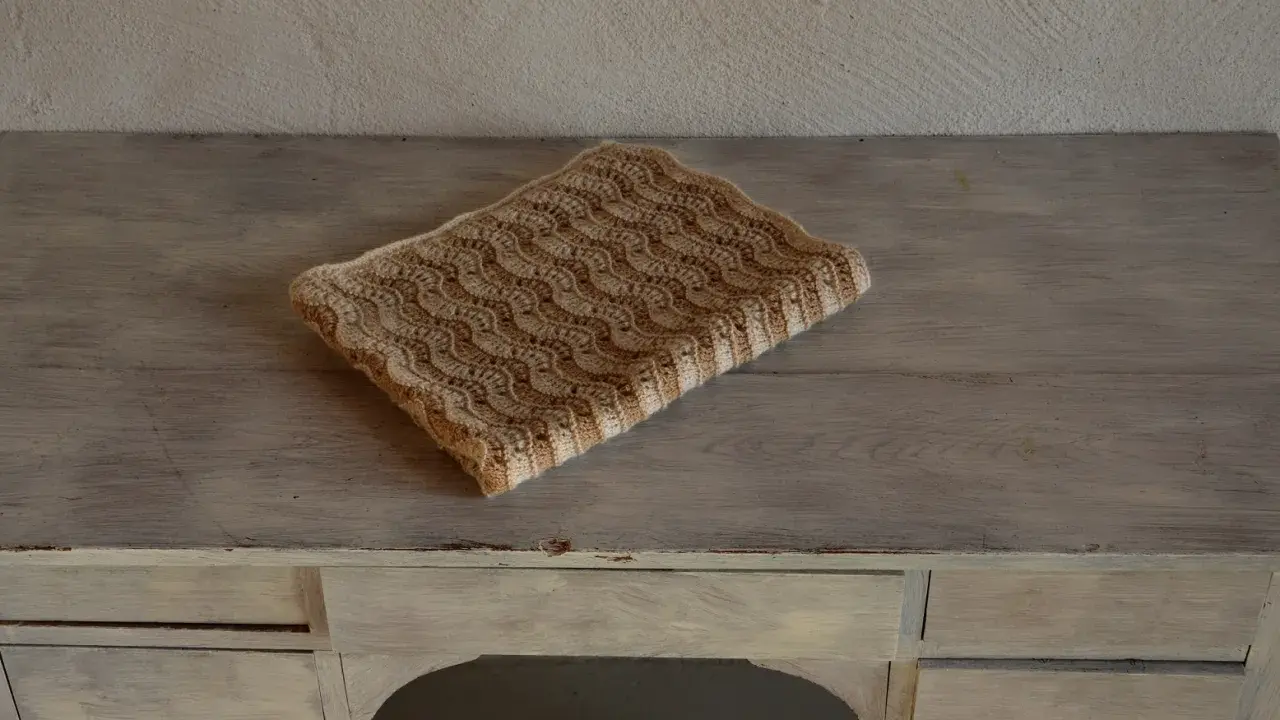 En vacker babyfilt stickad i ett vågmönster med ljusa och mörkare bruna nyanser.