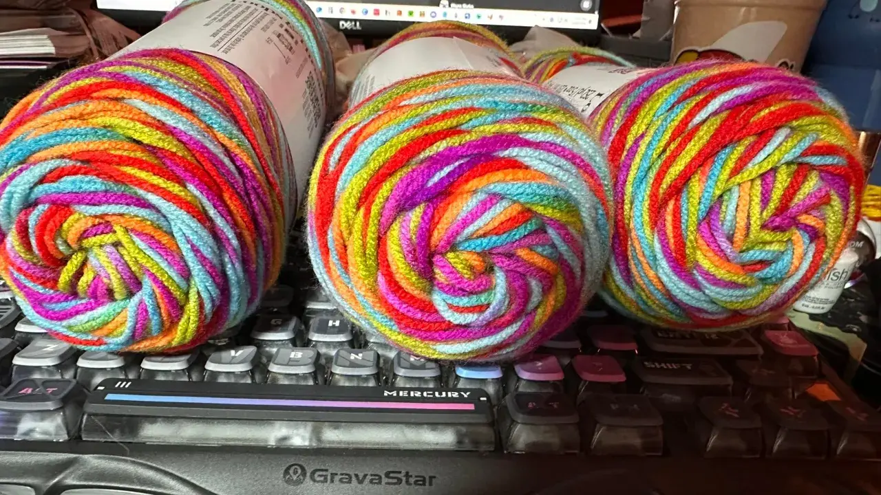 Three balls of brightly colored, variegated yarn sit on a keyboard.