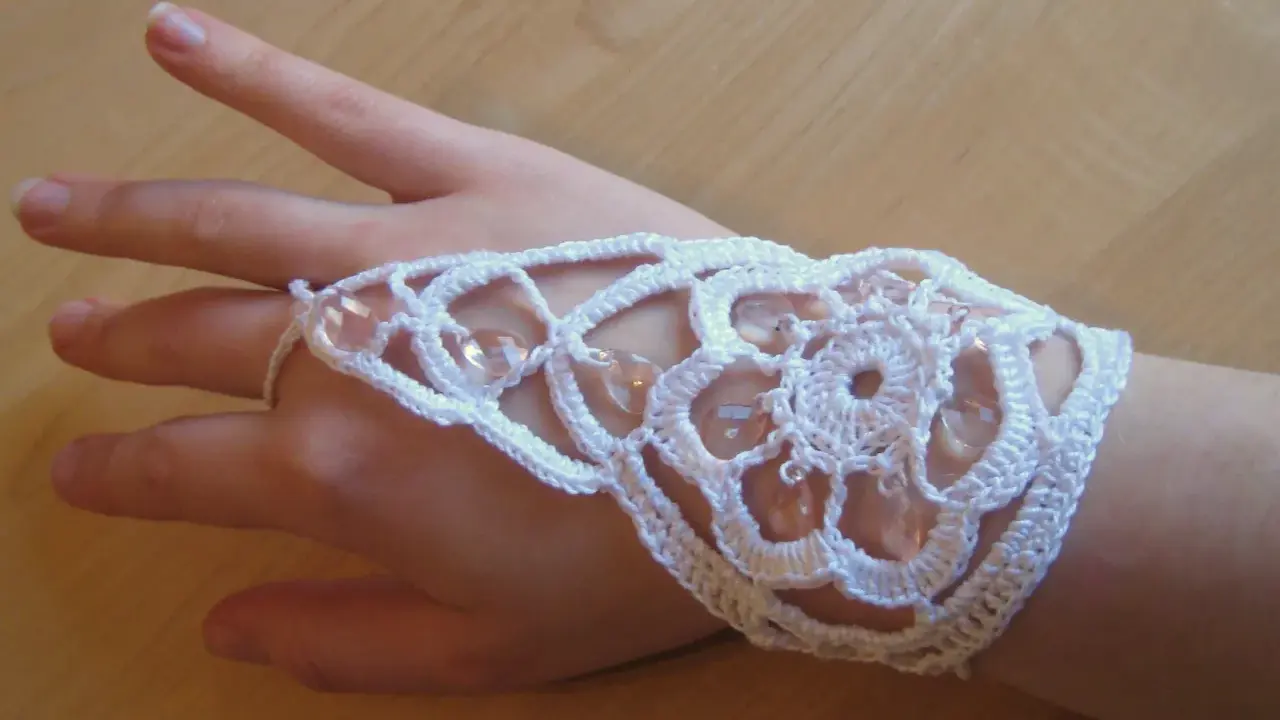 Ett vackert virkat armband i vitt med pärlor, som pryder en hand.