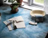 Två virka handdukar med blå ränder ligger på ett blått bord. En krukväxt och en skål syns också.