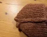Bruna, sticka tovade tofflor ligger på ett träbord.