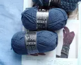Two balls of dark blue yarn and a knitted glove with a floral pattern.