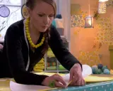 Kvinna med gult halsband mäter tyg för att sy topp.