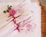 Vita tygservetter med rosa blommor, bundna med rosa snöre och dekorerade med en ros. Vackert dukat för en sommarfest.