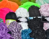 A colorful assortment of yarn balls in various textures and colors, including purple, pink, orange, green, white, black, and blue.