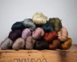A pile of colorful yarn skeins in various earthy tones, resting on a wooden crate.