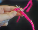 En hand håller stickor och ljusrosa garn, redo att starta stickning.