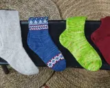 Fyra par handstickade sockor i olika färger och mönster. Perfekt för att sticka enkla sockor till barn.