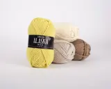 Gula, beige, ljusbruna och vita nystan av Drops Alaska garn ligger i en hög.