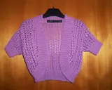 A purple crocheted bolero with short sleeves and an openwork pattern hangs on a hanger against a wooden background.