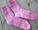 Två par randiga sockor i rosa och lila toner ligger på en träyta.