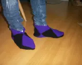 Ett par stickade innetofflor i lila och svart, med jeans till. Perfekta för mysiga hemmakvällar.