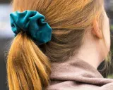 En hästsvans med en turkos scrunchie i sammet. Håret är kopparfärgat och faller mjukt.