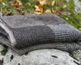 En hopvikt, handstickad filt i gråa nyanser ligger på en mossig sten. Perfekt för mysiga höstkvällar.