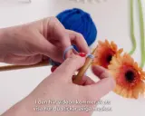 Händer stickar med garn och stickor. En blå garnboll och orange gerberor i bakgrunden. Lär dig stockinette stitch svenska.
