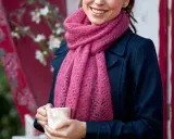 En kvinna ler och håller en mugg, insvept i en mjuk, rosa mohairhalsduk.