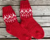 Två par röda, stickade strumpor med vitt mönster av hjärtan och snöflingor ligger på en träbänk. Perfekta för kalla dagar!