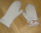 Två vita, stickade vantar med diskreta drops design-mönster i färggranna trådar på muddarna.
