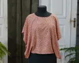 En persikofärgad blus med ett litet mönster av mörka prickar och små blommor. Blusen har en vid passform och korta, fladdermusliknande ärmar.