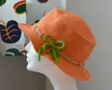 En orange virkad hatt med ljusgröna detaljer och en rosett. Perfekt för sommaren!