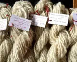 Buntar av ljusbeige garn, troligen mohair ull, med handskrivna etiketter som beskriver tvättmetoder och ursprung.