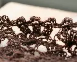Close-up of a brown, lacy crocheted fabric with an openwork pattern.