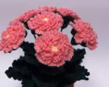 En bukett av virka blommor i rosa med gula mittar och mörkgröna blad.