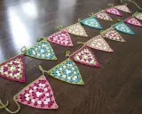 En lång rad med virka vimpel i rosa, vitt, grönt och blått ligger utspridda på ett mörkt trägolv.