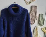 Mörkblå stickad polokrage med färgglada prickar, bredvid stickade vantar och en akvarellmålning av syrener.