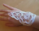 Ett vackert virkat armband i vitt med pärlor, som pryder en hand.