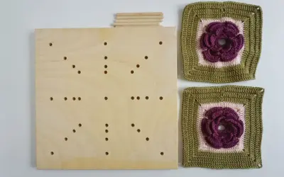 En träplatta med hål och pinnar, redo att användas som blockningsmatta för virkade blommor.