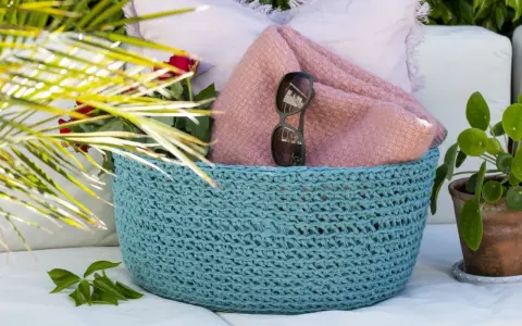 En turkos virkad korg med ett vackert virkmönster, fylld med en rosa filt, solglasögon och röda rosor.