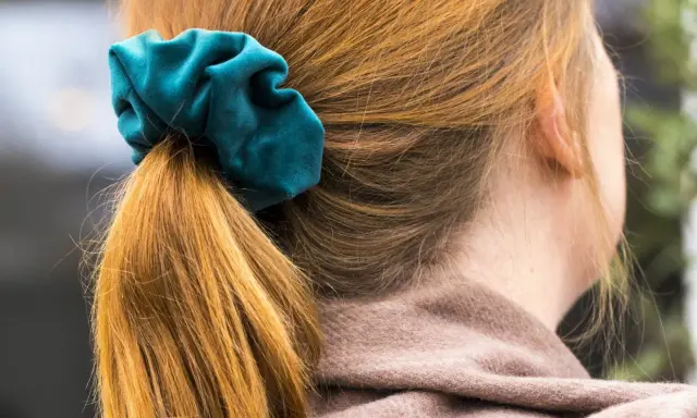 En hästsvans med en turkos scrunchie i sammet. Håret är kopparfärgat och faller mjukt.