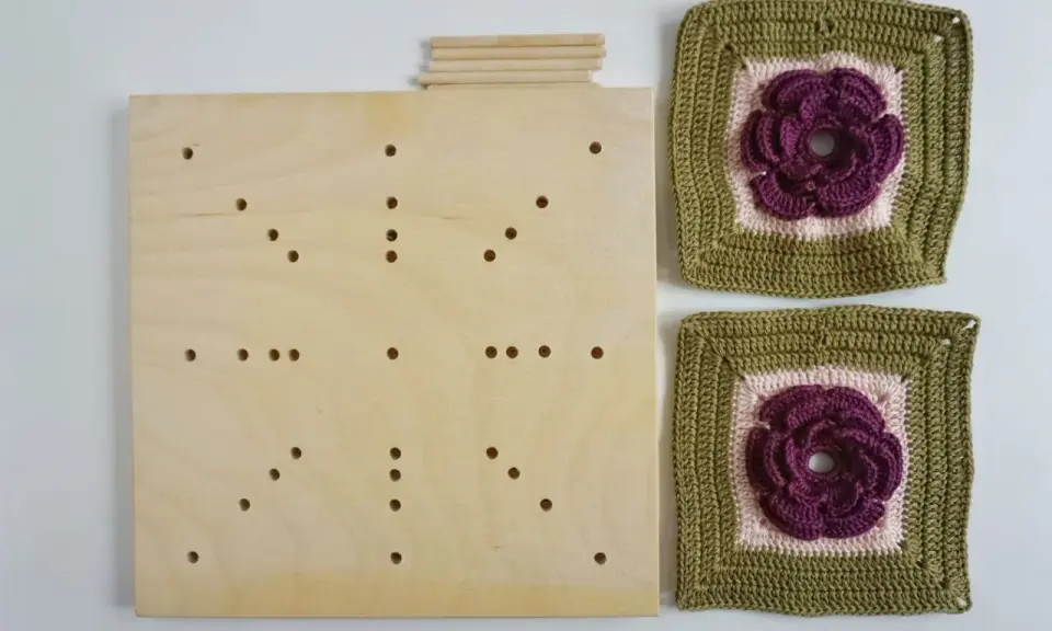 En träplatta med hål och pinnar, redo att användas som blockningsmatta för virkade blommor.